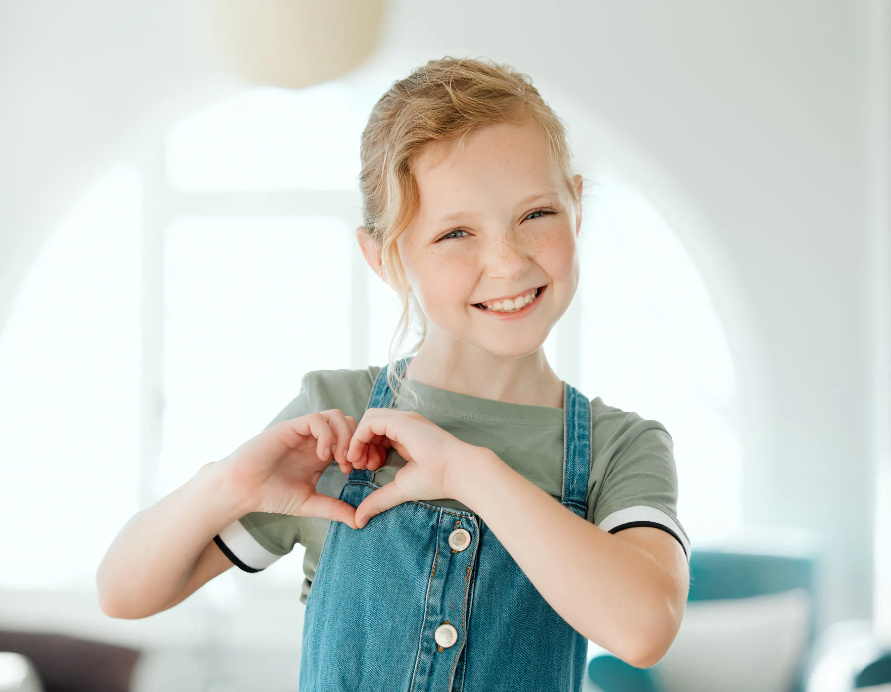 Child smiling and making a heart shape with her hands